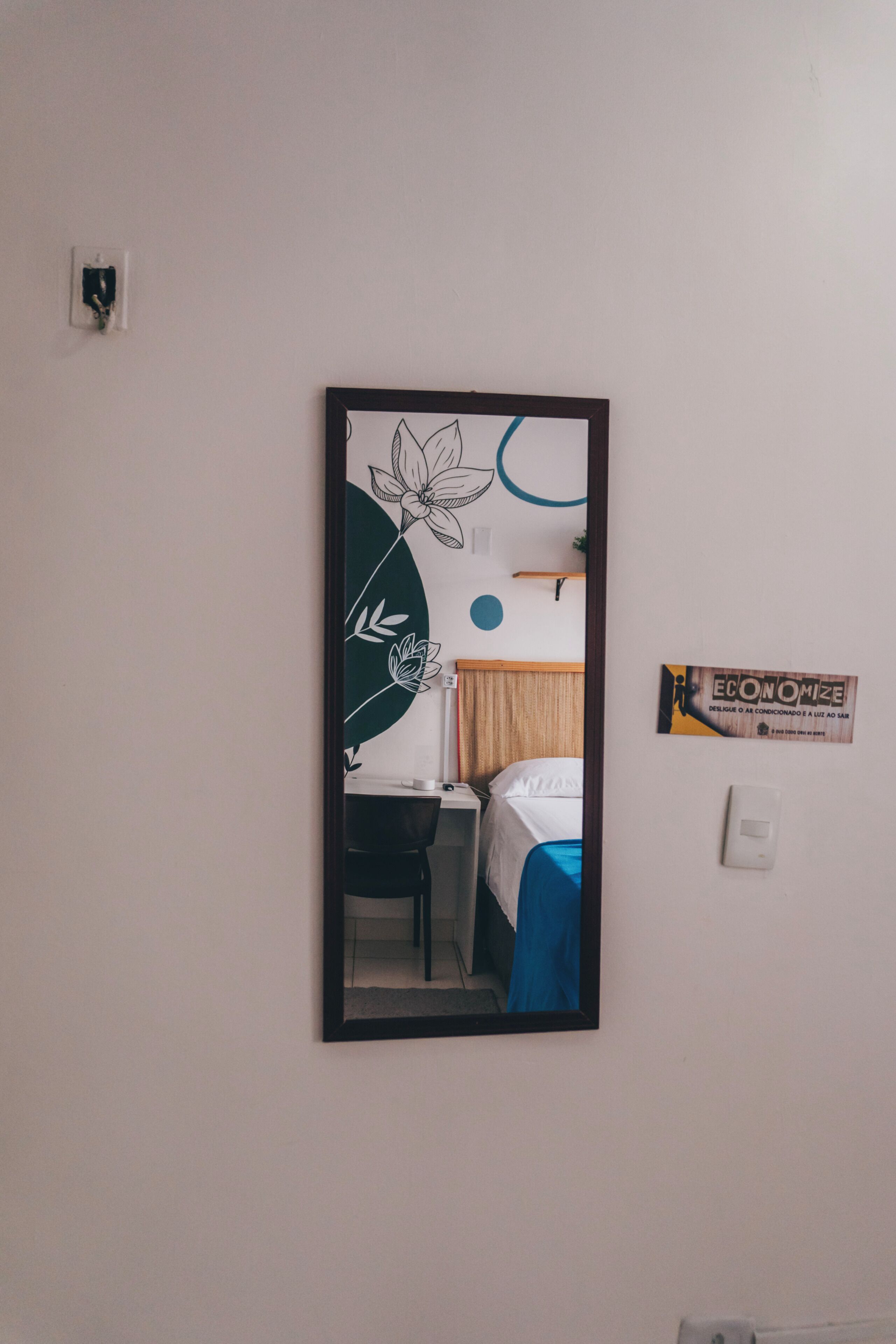 Un espejo refleja una habitación con cama, escritorio y silla.