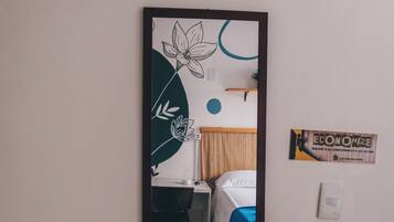 Un espejo refleja una habitación con cama, escritorio y silla.