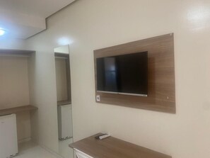 A room with a flat-screen TV mounted on a wooden panel, a small table with a remote control, and a mirror on the wall.
