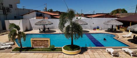 A swimming pool with a tiled deck, surrounded by lounge chairs and umbrellas.