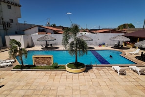 A swimming pool with a tiled deck, surrounded by lounge chairs and umbrellas.