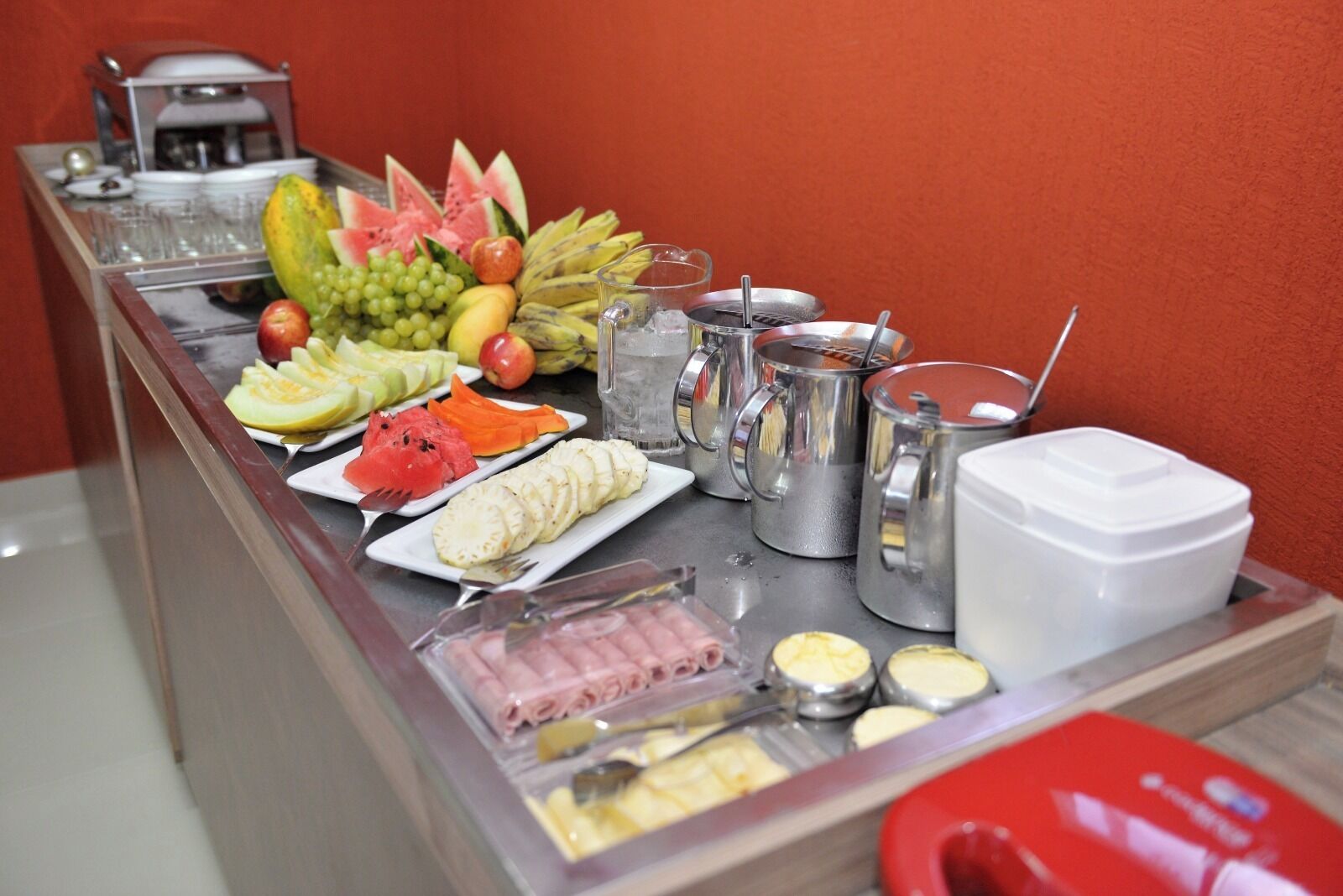 A buffet setup with various fruits, sliced meats, and beverages.