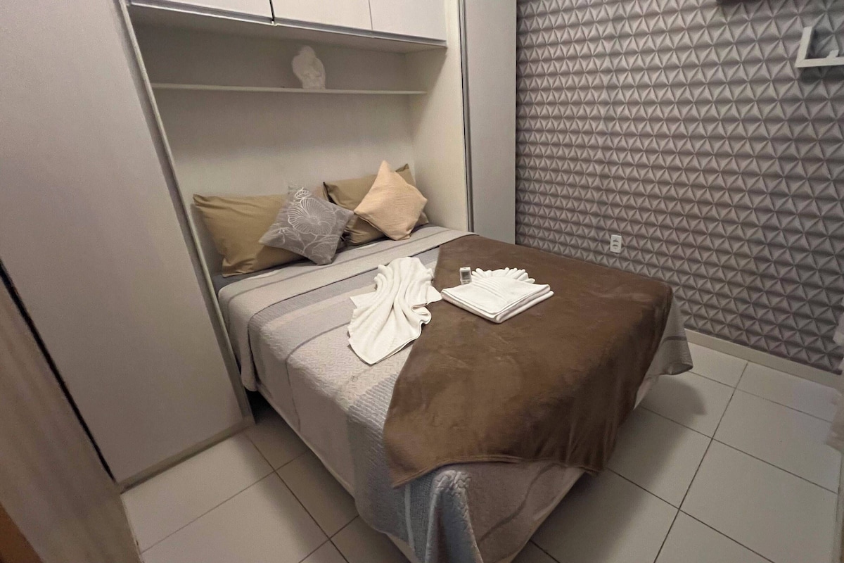 Hotellihuone, jossa on sänky, tyynyjä, ruskea peitto ja taitettu valkoinen pyyhe.