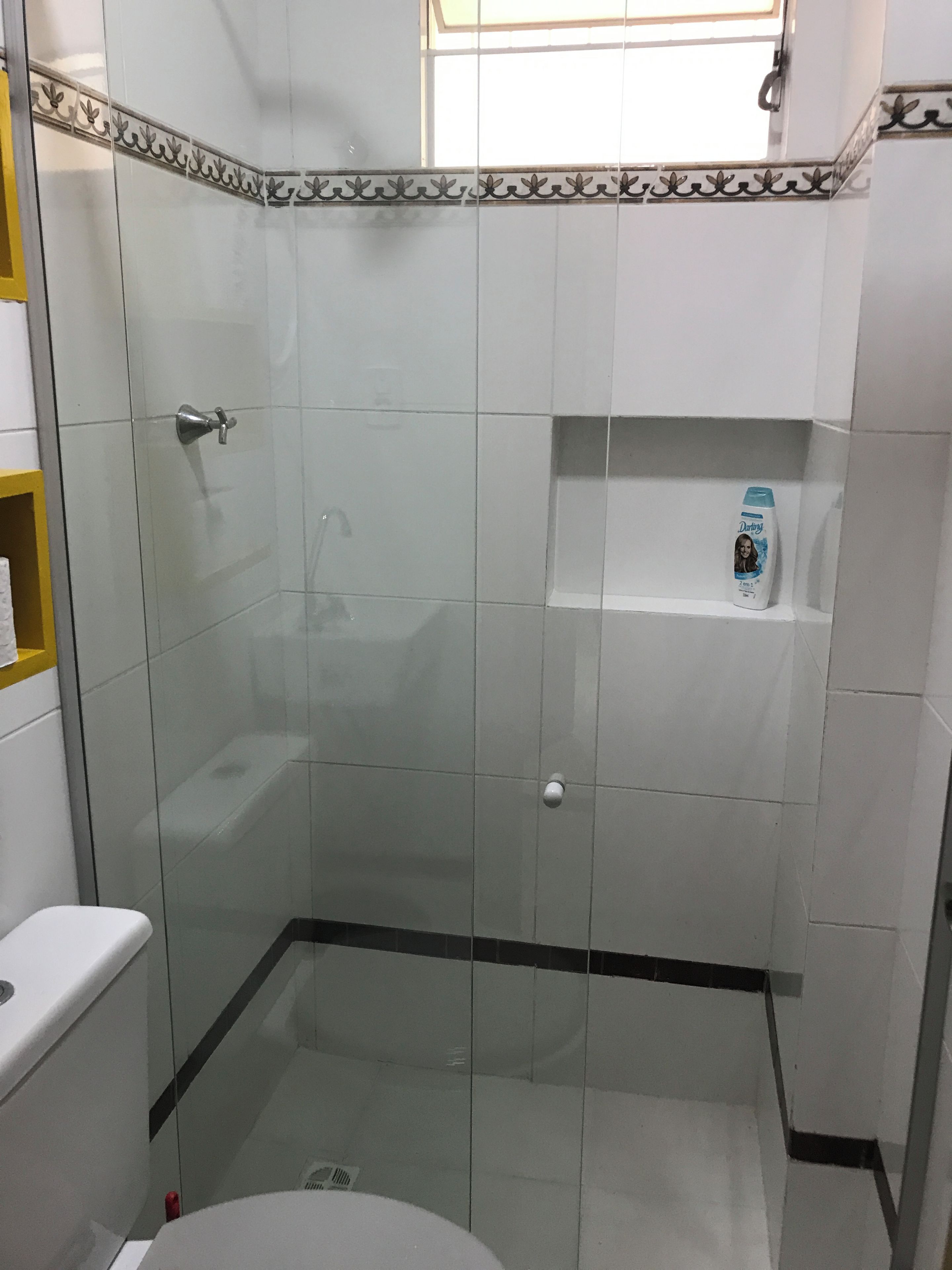 A bathroom with a glass-enclosed shower, a toilet, and a shelf with a bottle.