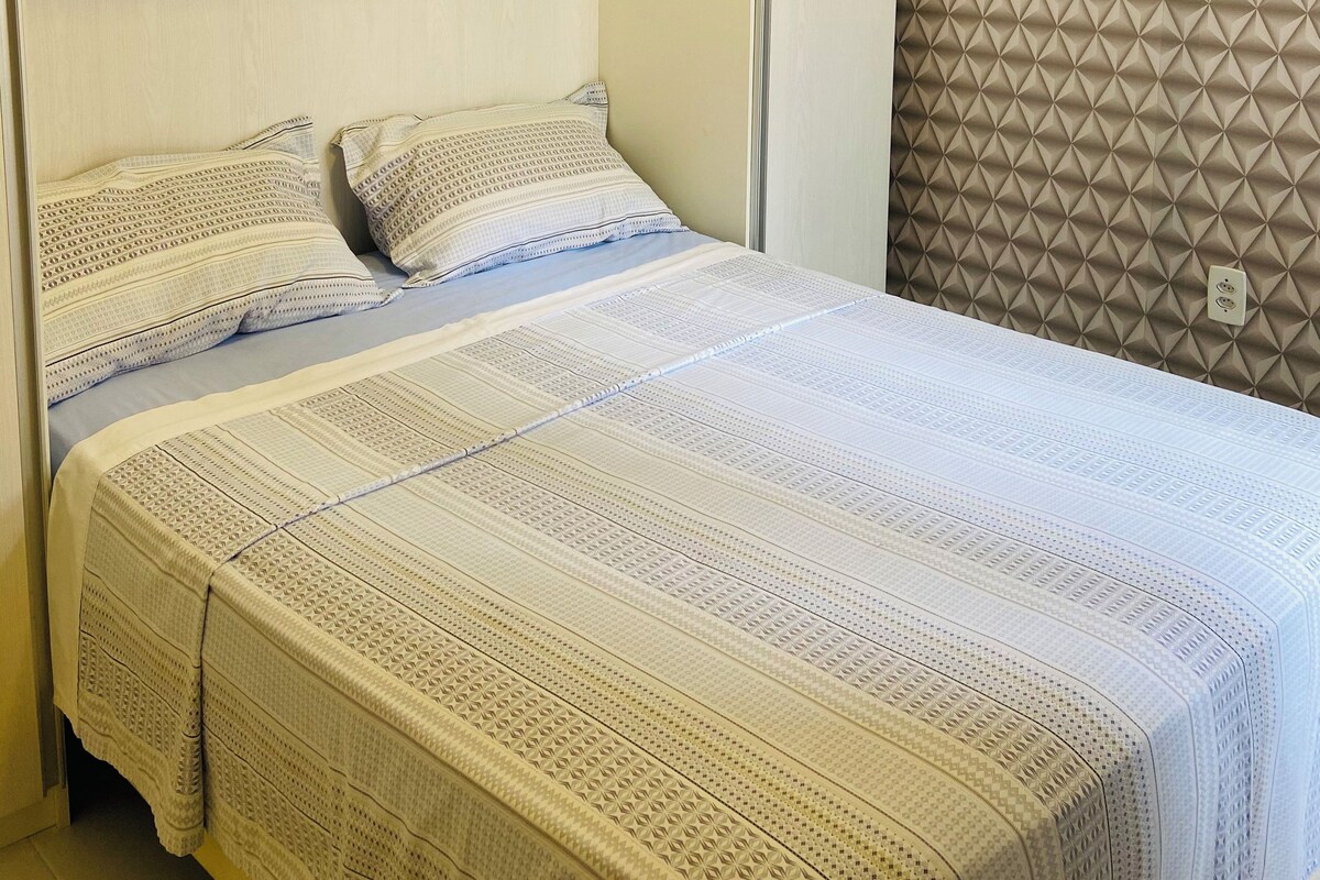 A bedroom with a bed, pillows, a wardrobe, and a textured wall.