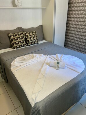 A neatly made bed with a white blanket and a towel, a grey sofa with patterned cushions, and a textured wall behind the sofa. - 104 Apartamento lindo e delicado (Belém)