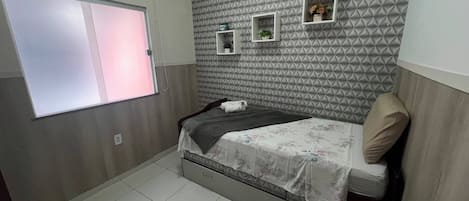 A small bedroom with a bed, a window, and a wall with geometric patterns.