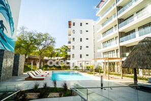 A modern hotel with a swimming pool, lounge chairs, and a thatched-roof structure. - The Drifter • 2Bdr • Ocean View & Steps to Surf (El Zonte)