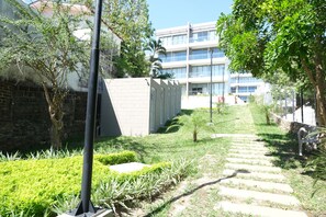 A pathway leading to a building with a modern design, surrounded by greenery and a stone wall. - The Drifter • 2Bdr • Ocean View & Steps to Surf (El Zonte)
