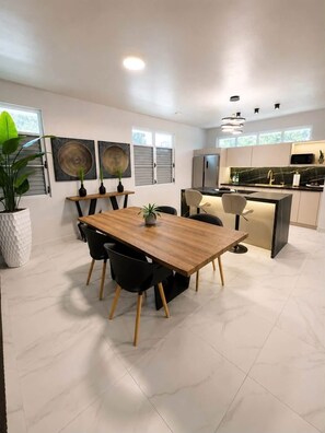 Una cucina moderna con zona pranzo, con un tavolo in legno, sedie nere e pavimento piastrellato di bianco.