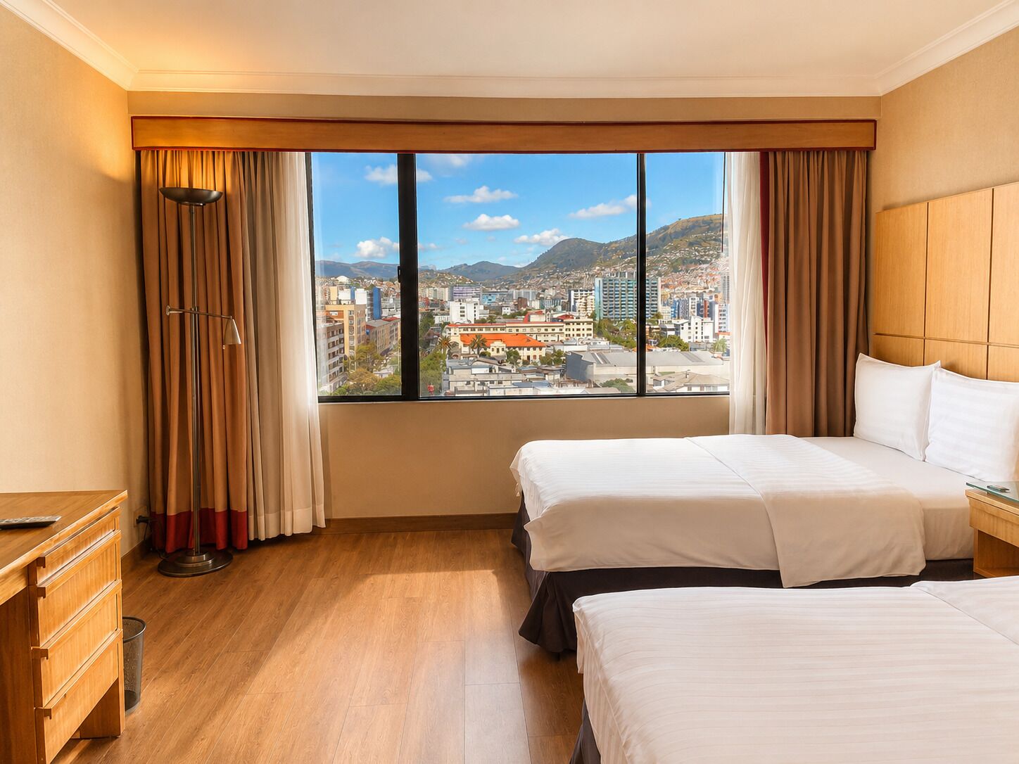 Una camera d'albergo con due letti, una scrivania e un'ampia finestra con vista sulla città.