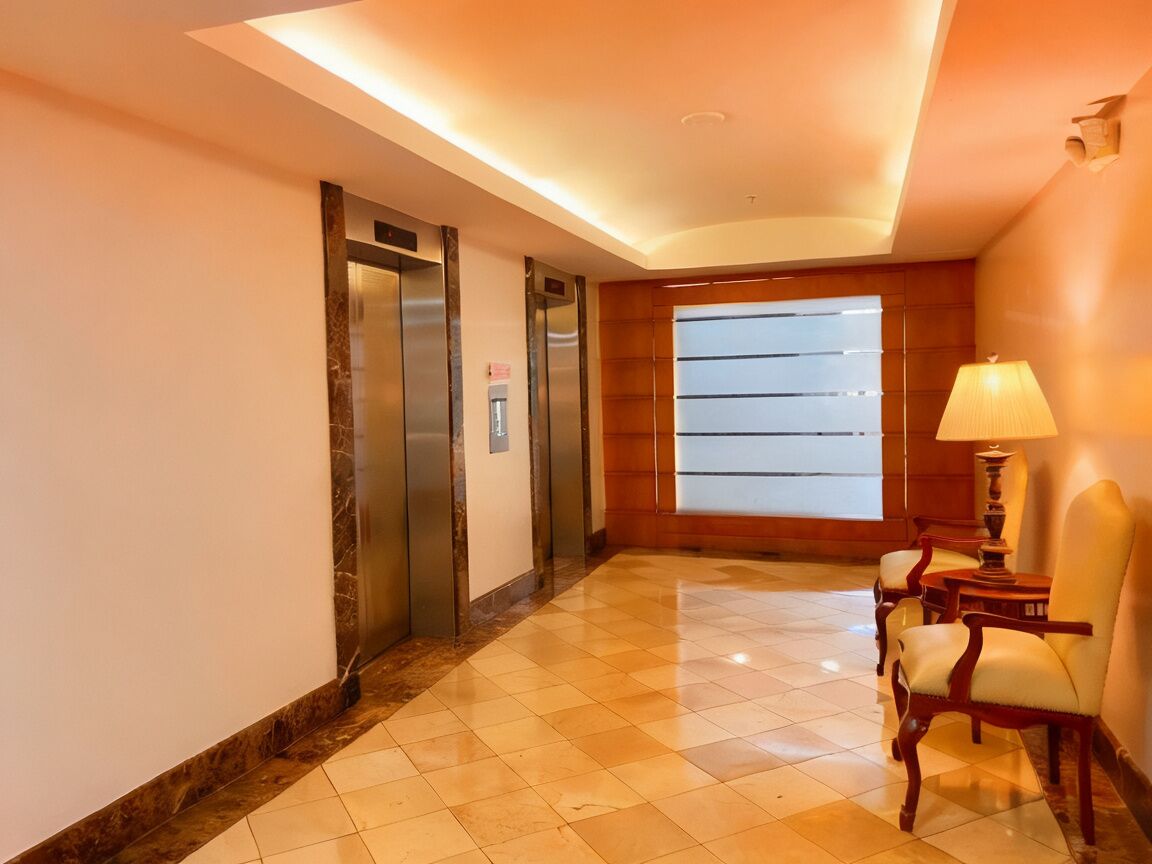 A hotel lobby with two elevators, a large window, and a seating area with a lamp.