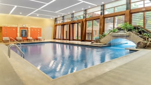 Une piscine intérieure bordée de pierres, dotée d’une terrasse en bois et offrant une vue sur l’extérieur grâce à de grandes fenêtres.