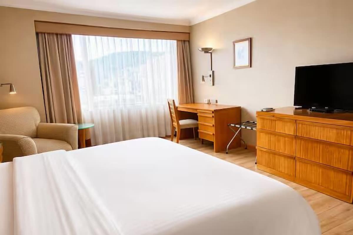 Une chambre d’hôtel avec un grand lit, un bureau, une chaise, une télévision et une armoire.