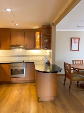 Cocina compacta con electrodomésticos integrados, comedor con mesa y sillas, y un cuadro enmarcado en la pared.