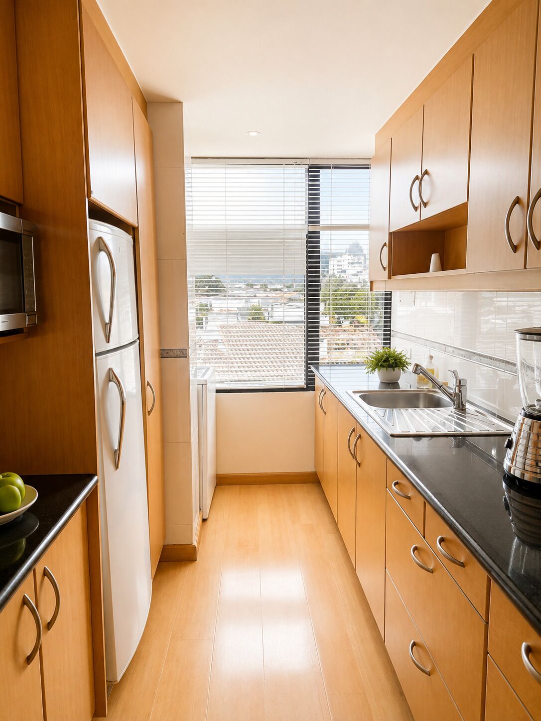 Una cocina moderna con armarios de madera, encimera negra, microondas integrado y ventana con persianas.