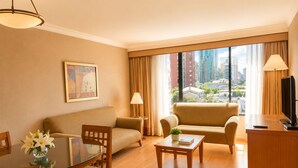 Habitación de hotel con sofá, una mesa de comedor, televisión y un ventanal con vistas a la ciudad.