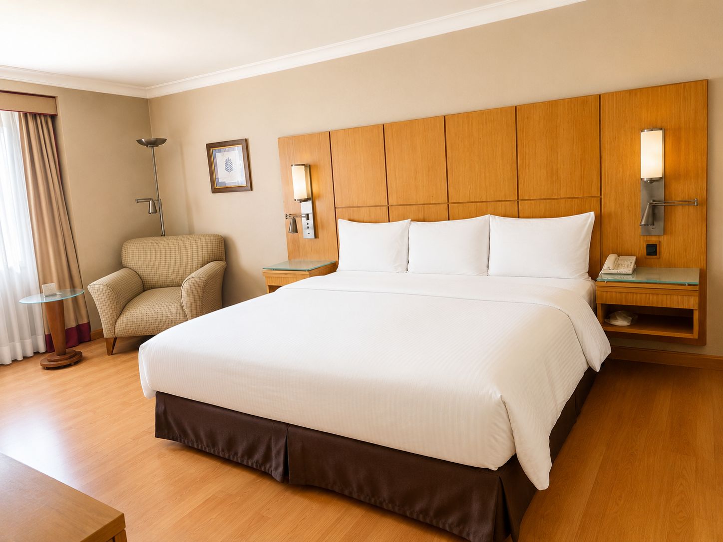 Habitación de hotel con una cama grande, una silla, una mesita de noche con lámpara y un teléfono en la pared.