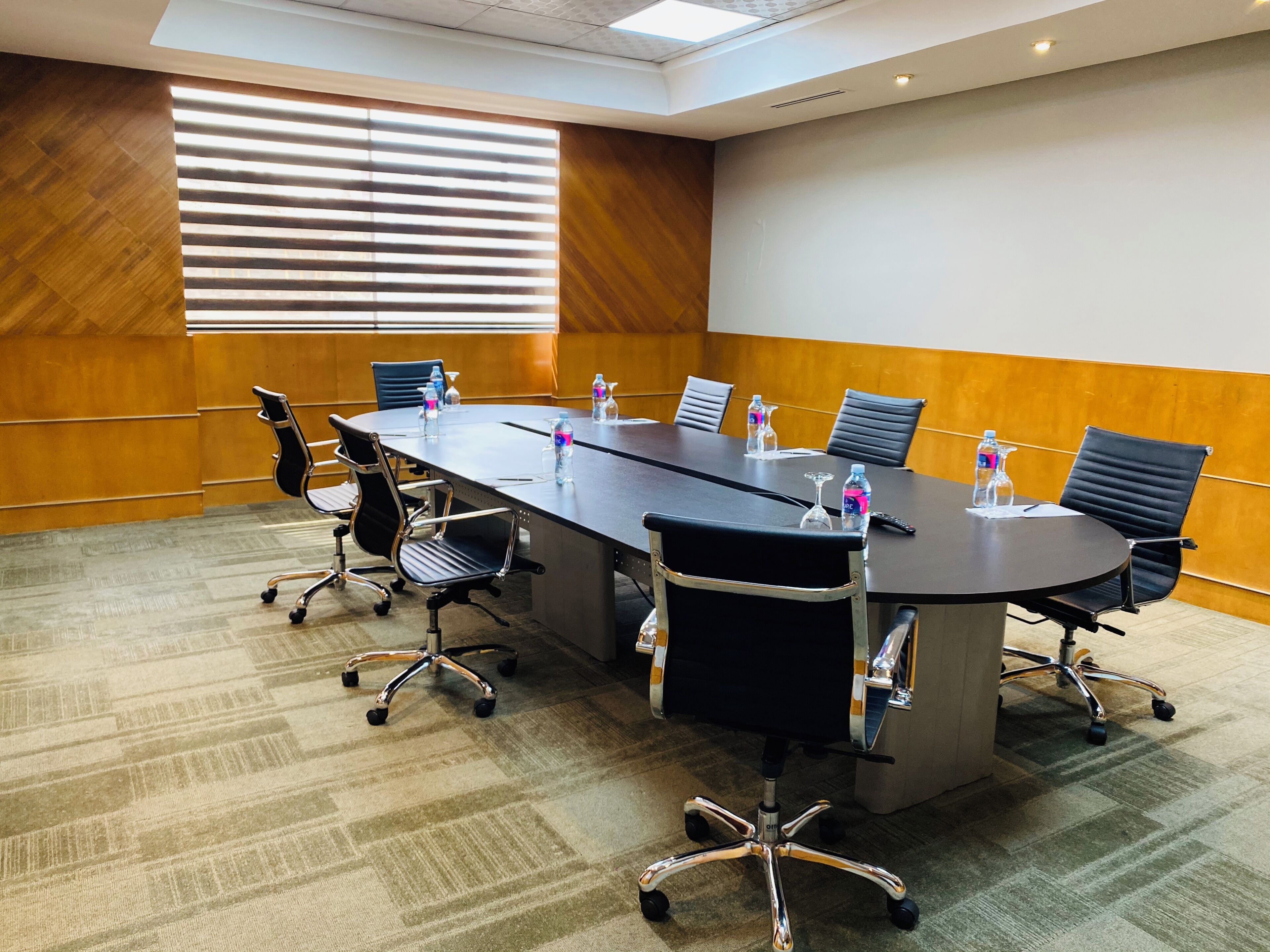 Un salón de conferencias con una mesa larga, seis sillas y botellas de agua.