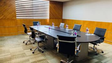 Un salón de conferencias con una mesa larga, seis sillas y botellas de agua.