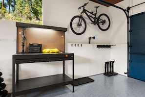 A workshop area with a pegboard wall, a workbench, and a bicycle mounted above.