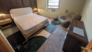 Une chambre à coucher comprenant un lit, des tables de chevet, un bureau, une chaise, une fenêtre et une lampe.