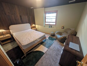 Et soveværelse med seng, natborde, skrivebord, stol, et vindue og en lampe.