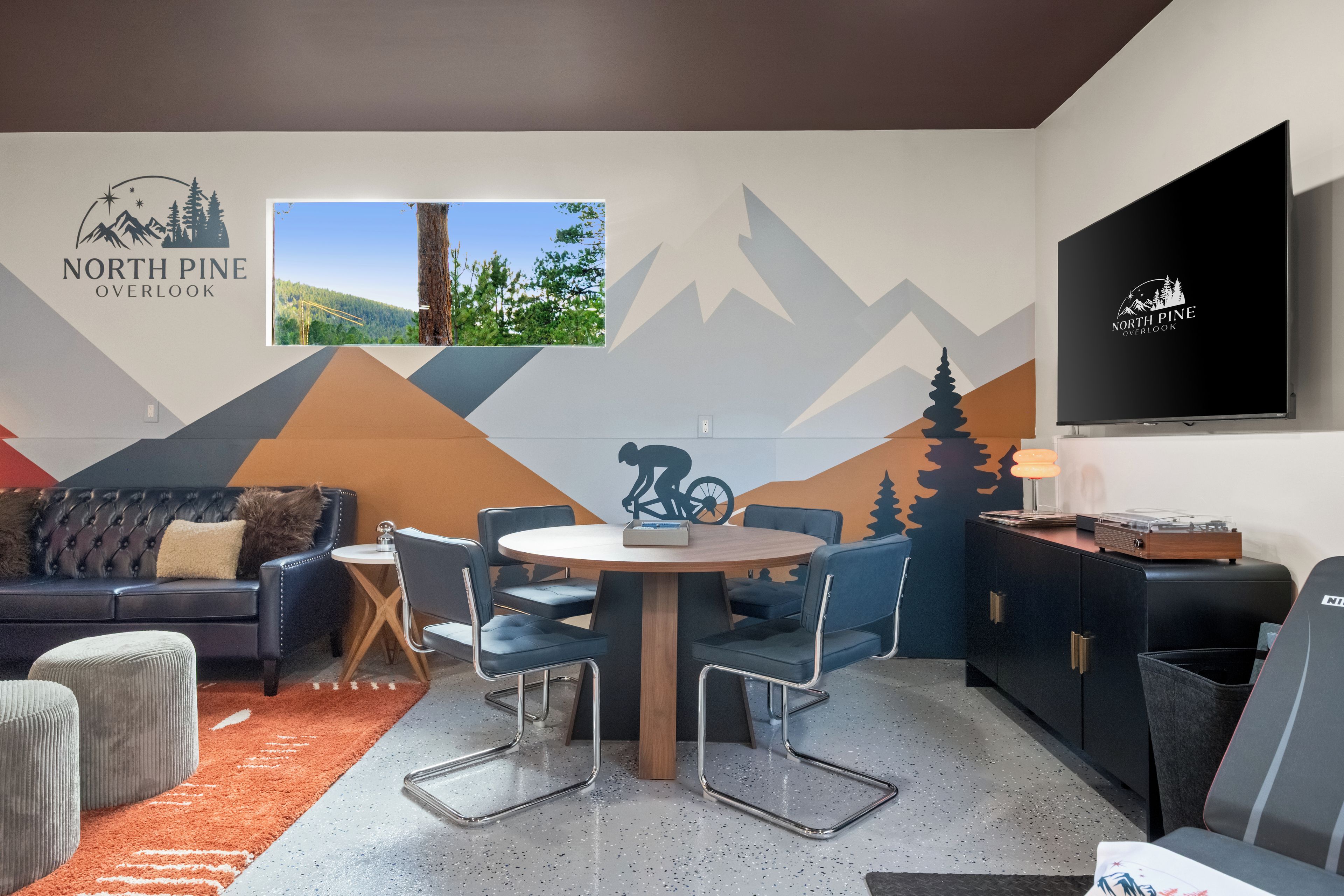 A modern living room with a mountain-themed wall mural, a flat-screen TV, a dining table with chairs, a sofa, and a coffee table.