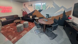 Une pièce comprenant un canapé, une table ronde et une fresque murale représentant des montagnes et un cycliste.
