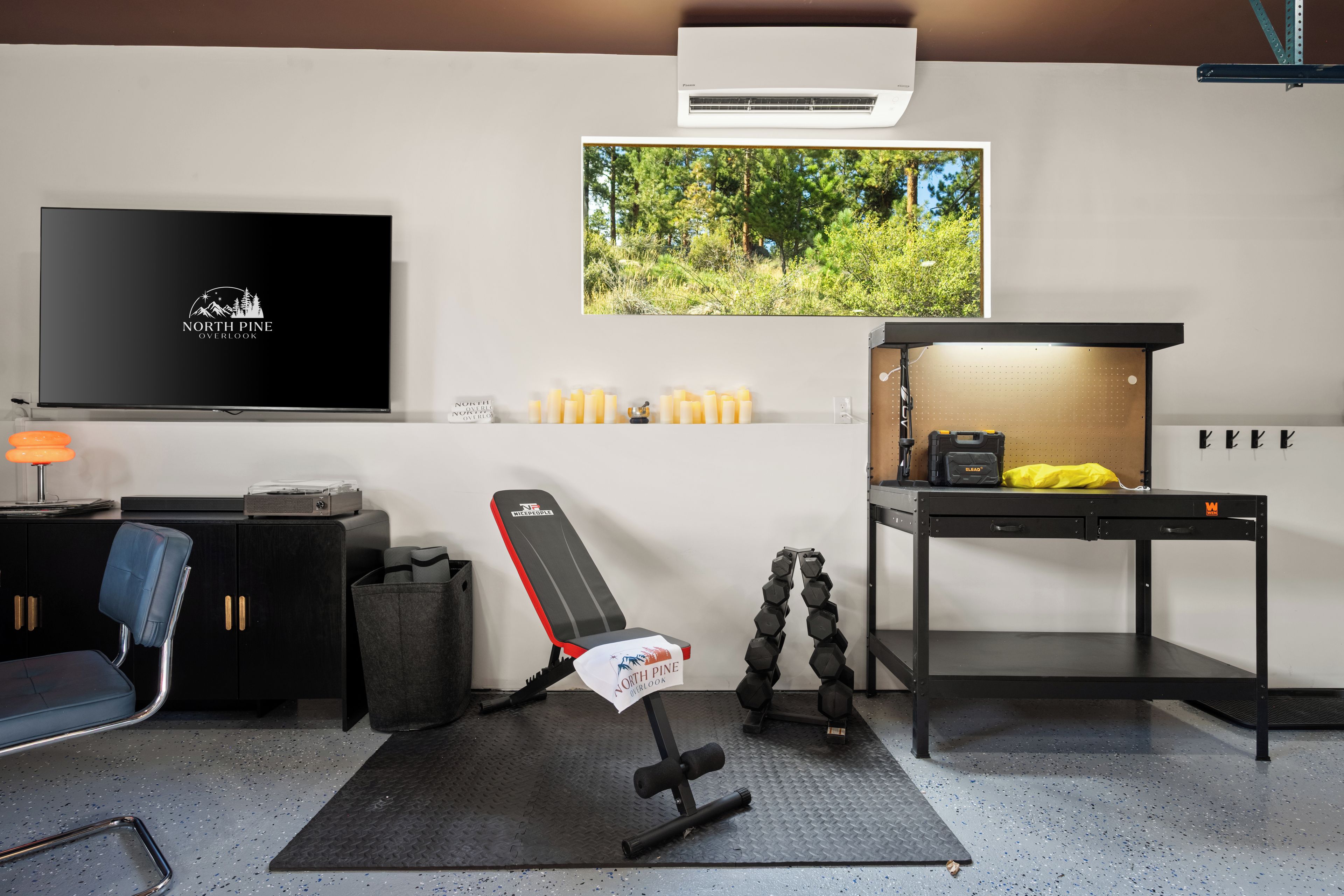 A modern home gym with a TV, exercise equipment, and a view of trees.
