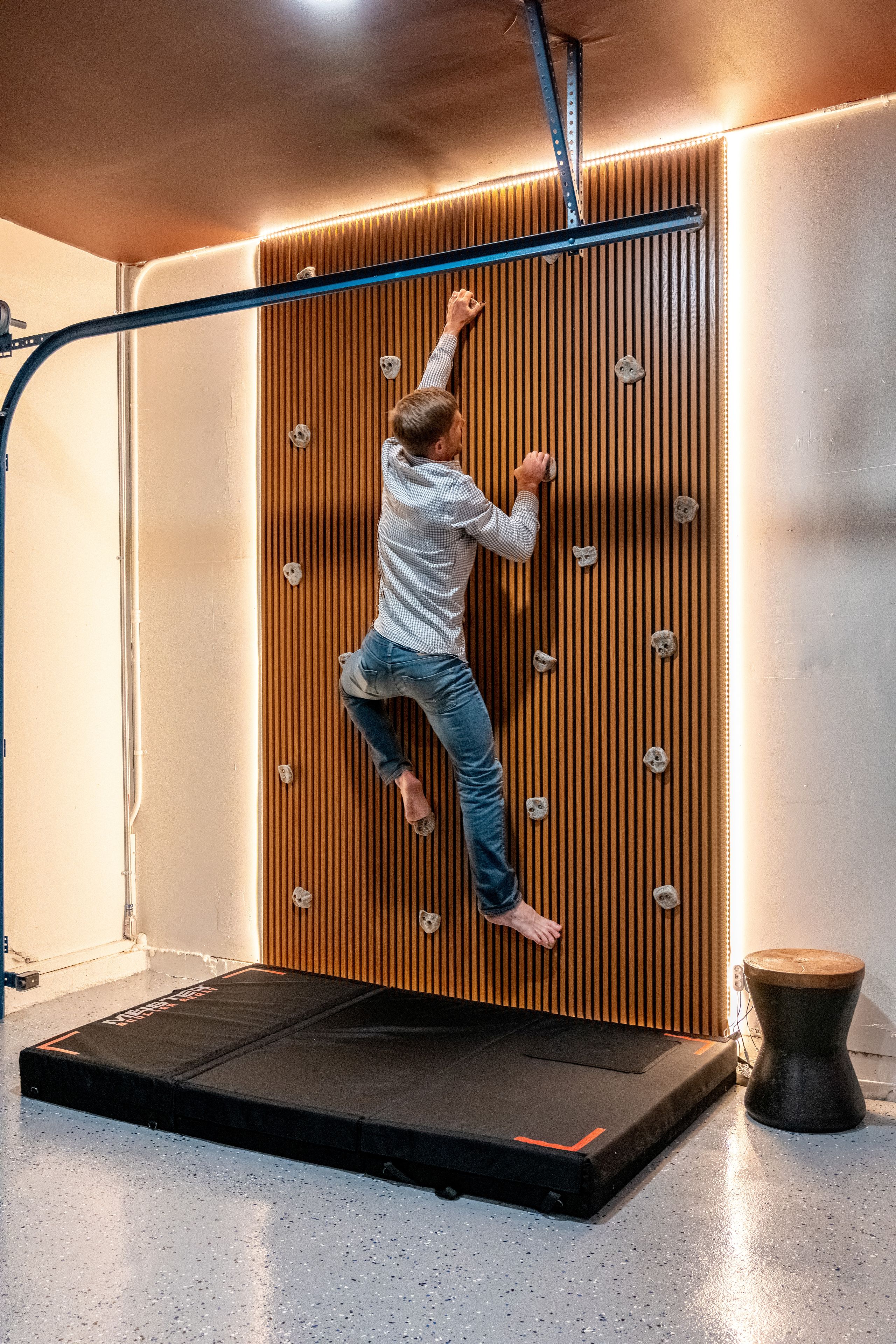 A person climbing a wooden wall with vertical slats and climbing holds.