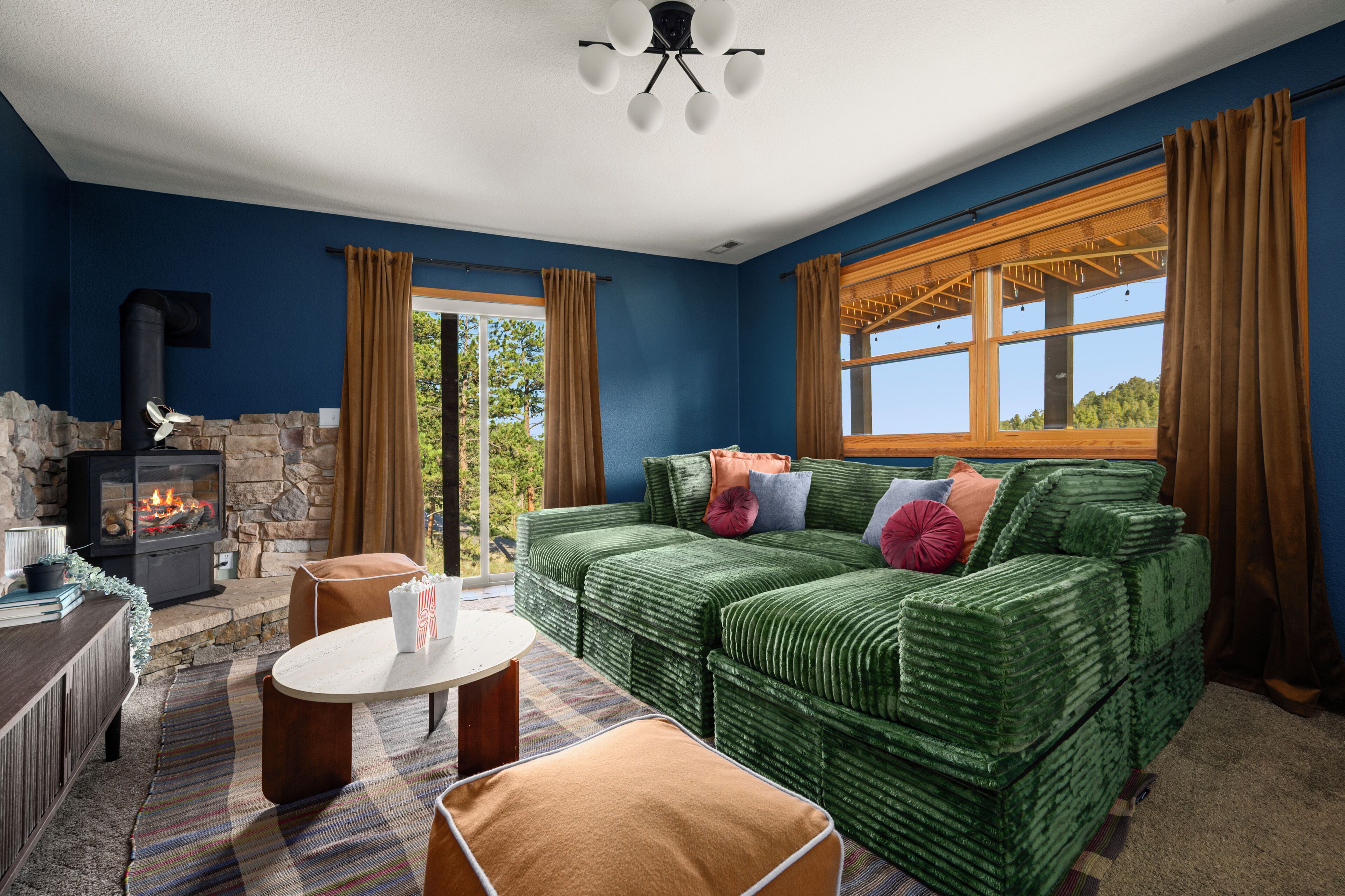 A cozy living room with a fireplace, a green sofa, a coffee table, and a view of the outdoors.