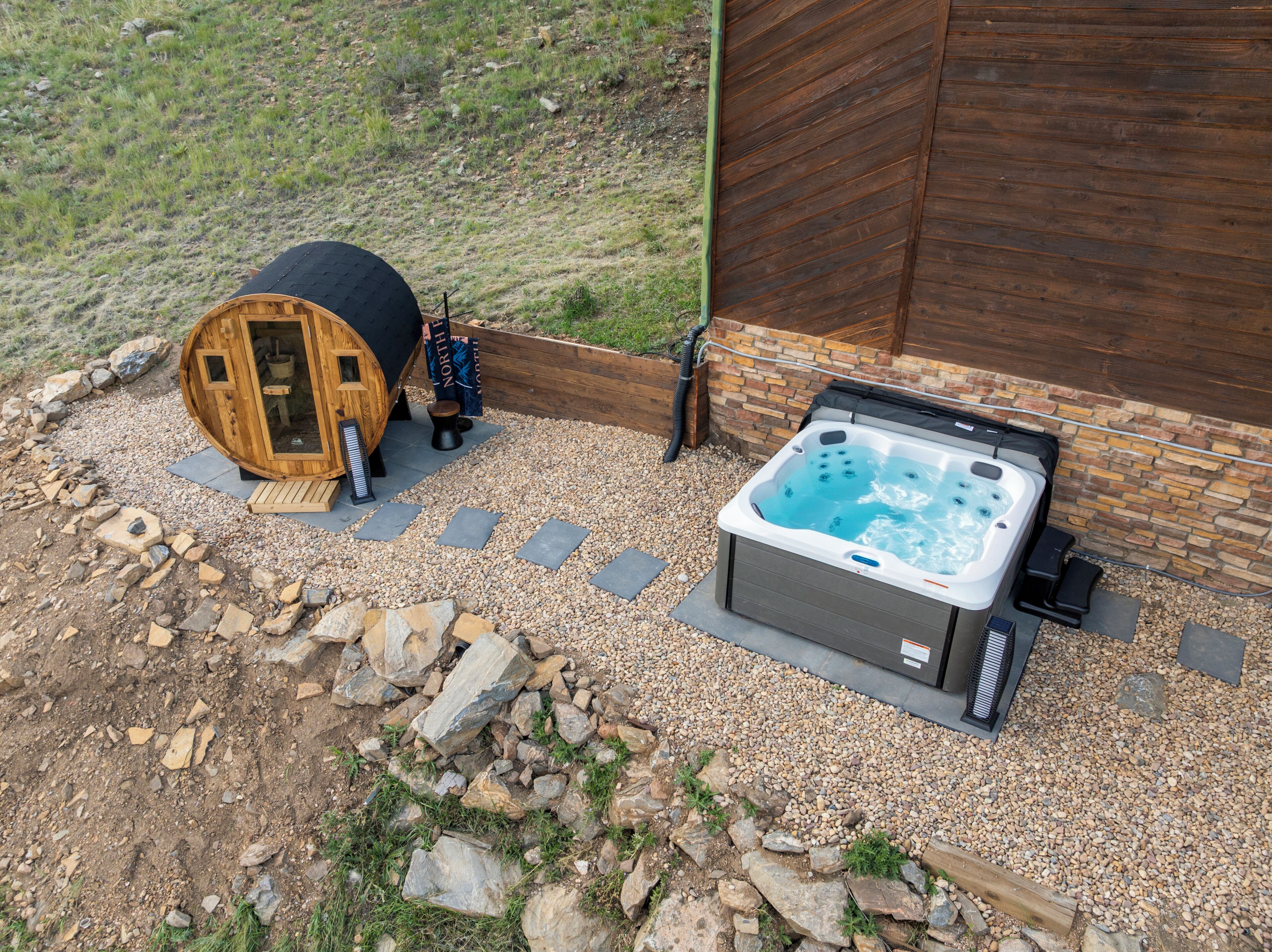 Een jacuzzi en een houten constructie met een ladder, omgeven door grind en stenen.