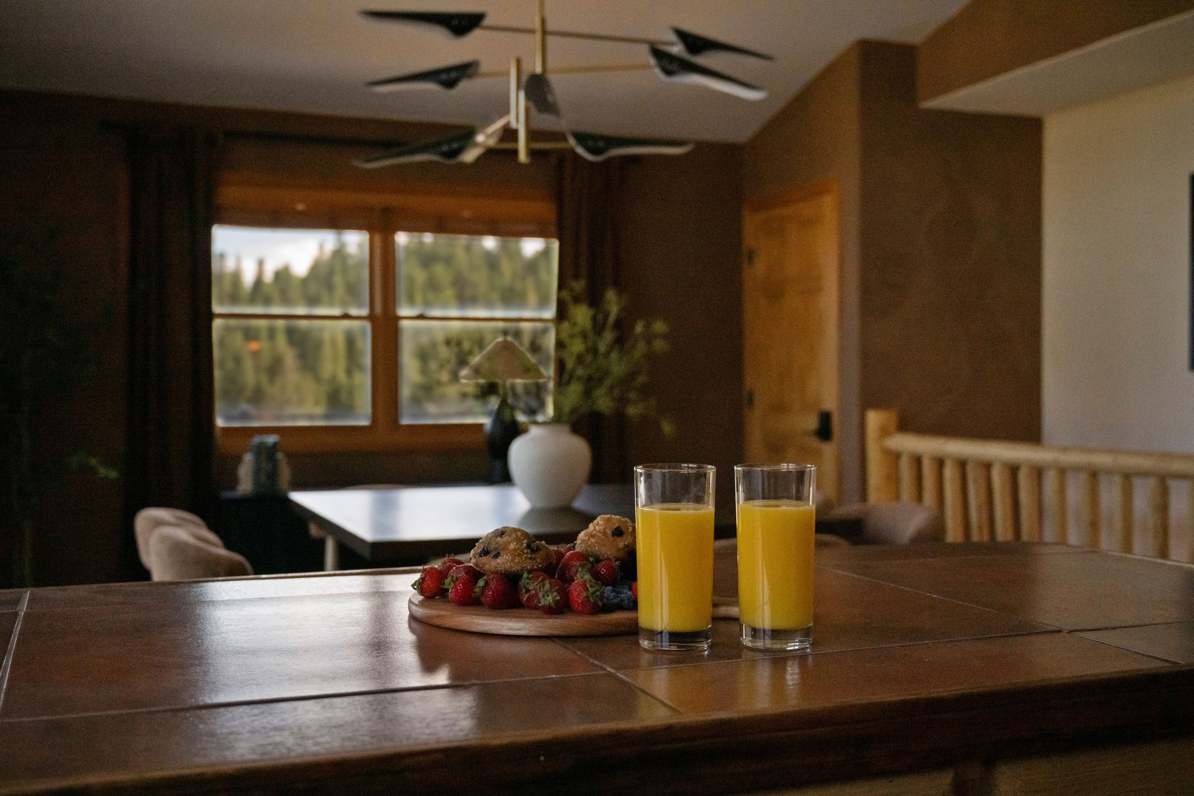A wooden table with two glasses of orange juice and a plate of strawberries and muffins.