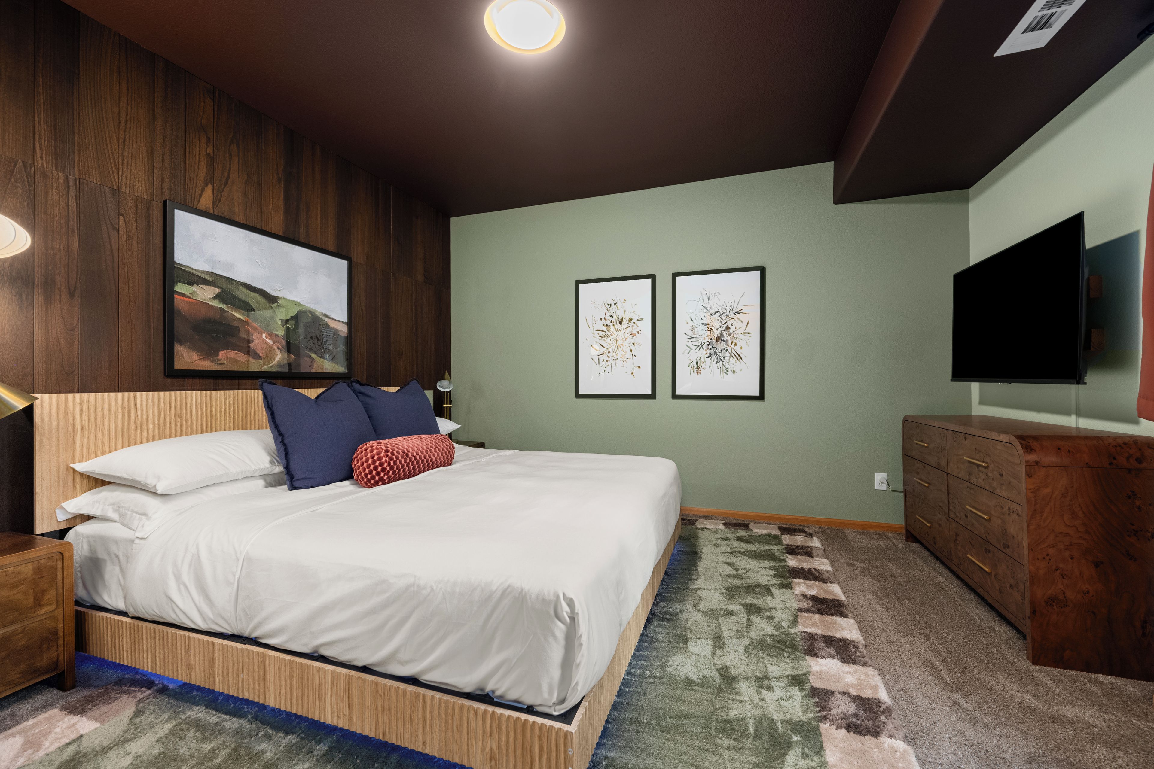 Een slaapkamer met een bed, nachtkastje, dressoir en een flatscreen televisie aan de muur.
