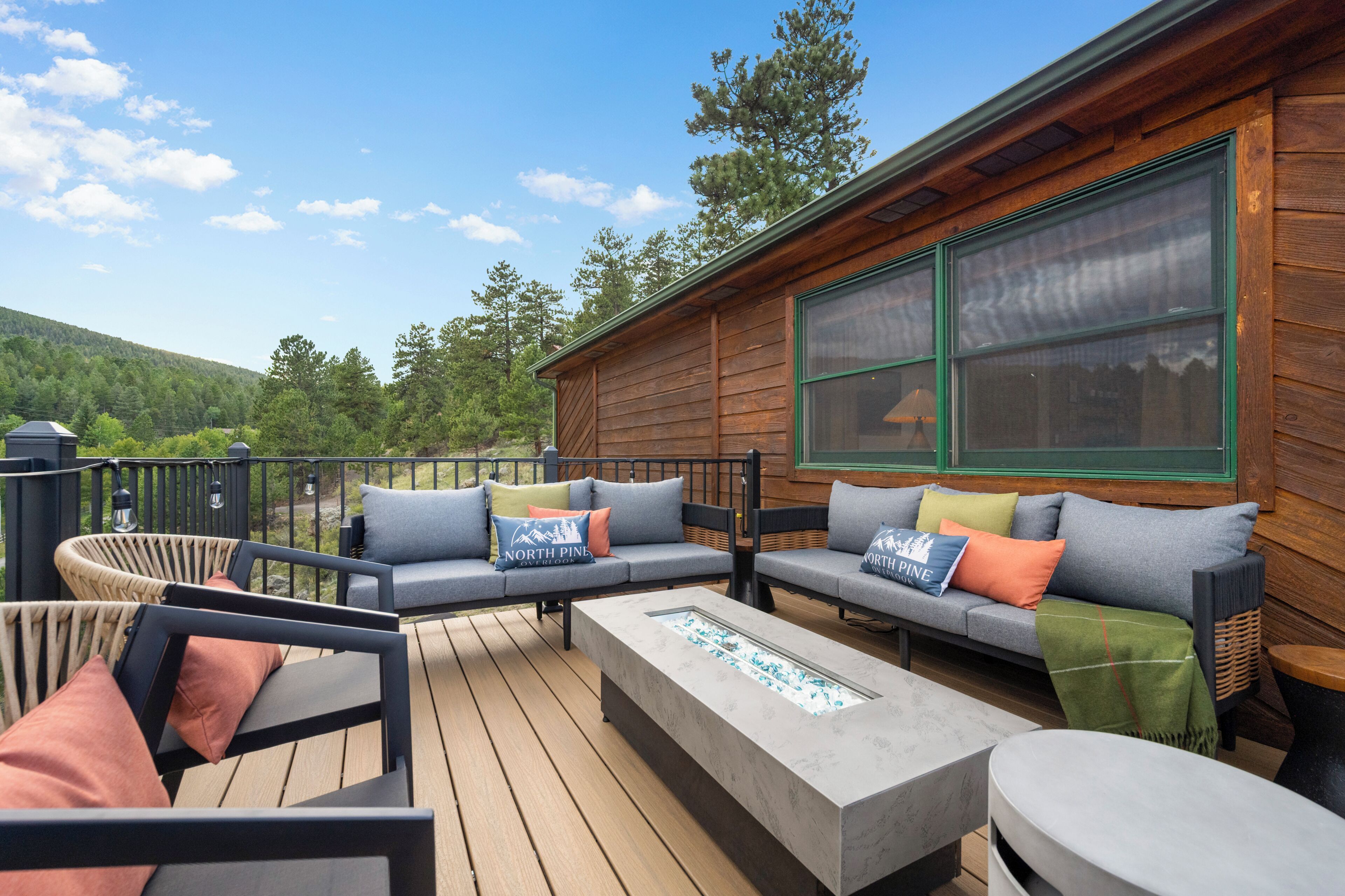 A wooden deck with outdoor furniture, including a sofa and chairs, and a large window on the cabin wall.