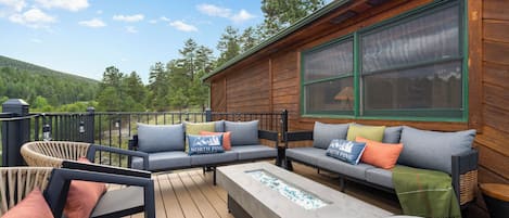 A wooden deck with outdoor furniture, including a sofa and chairs, and a large window on the cabin wall.