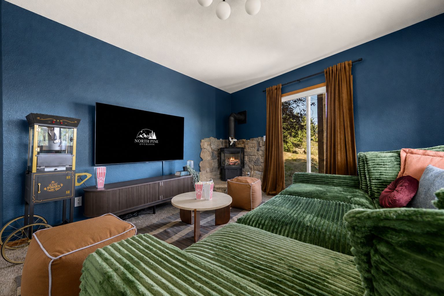 Una sala de estar acogedora con televisor de pantalla plana, máquina para hacer palomitas de maíz, chimenea de piedra y un conjunto de sofá verde.