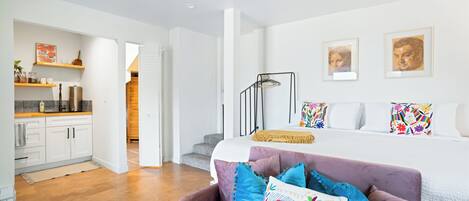 Une chambre moderne avec un lit, des coussins colorés, une table de chevet et une commode.