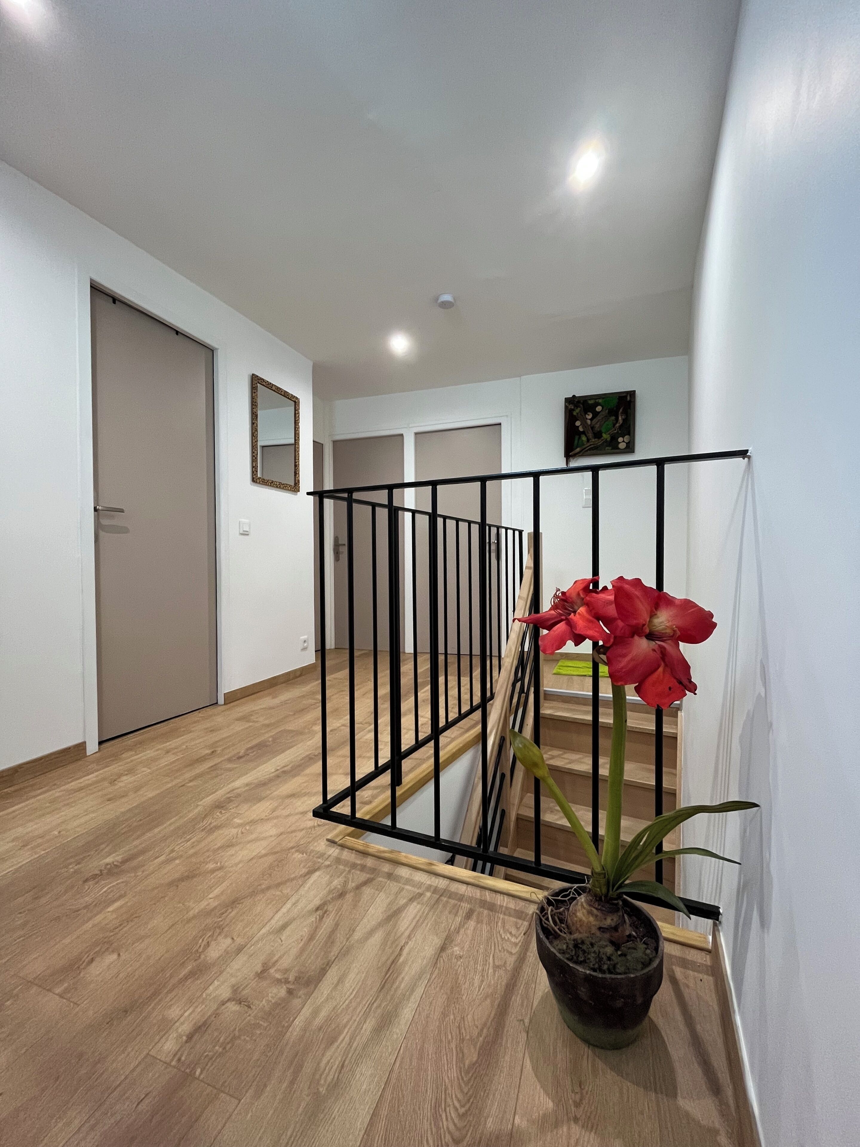A hallway with a wooden floor, a staircase with a black railing, and a potted plant with a red flower.