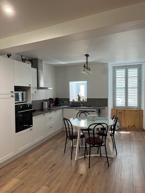 A modern kitchen with white cabinetry, a dining table with chairs, and a window with blinds. - Le Cazal Vacation Rental (Saint Geniez d'Olt et d'Aubrac)