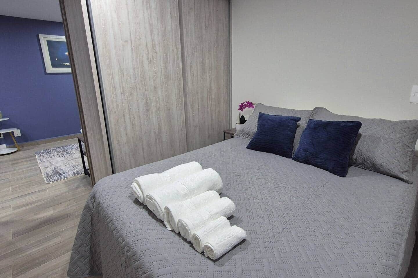 Un lit bien fait, avec une couette grise, deux oreillers et une serviette blanche enroulée.