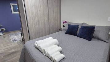 A neatly made bed with a grey quilt, two pillows, and a rolled white towel.