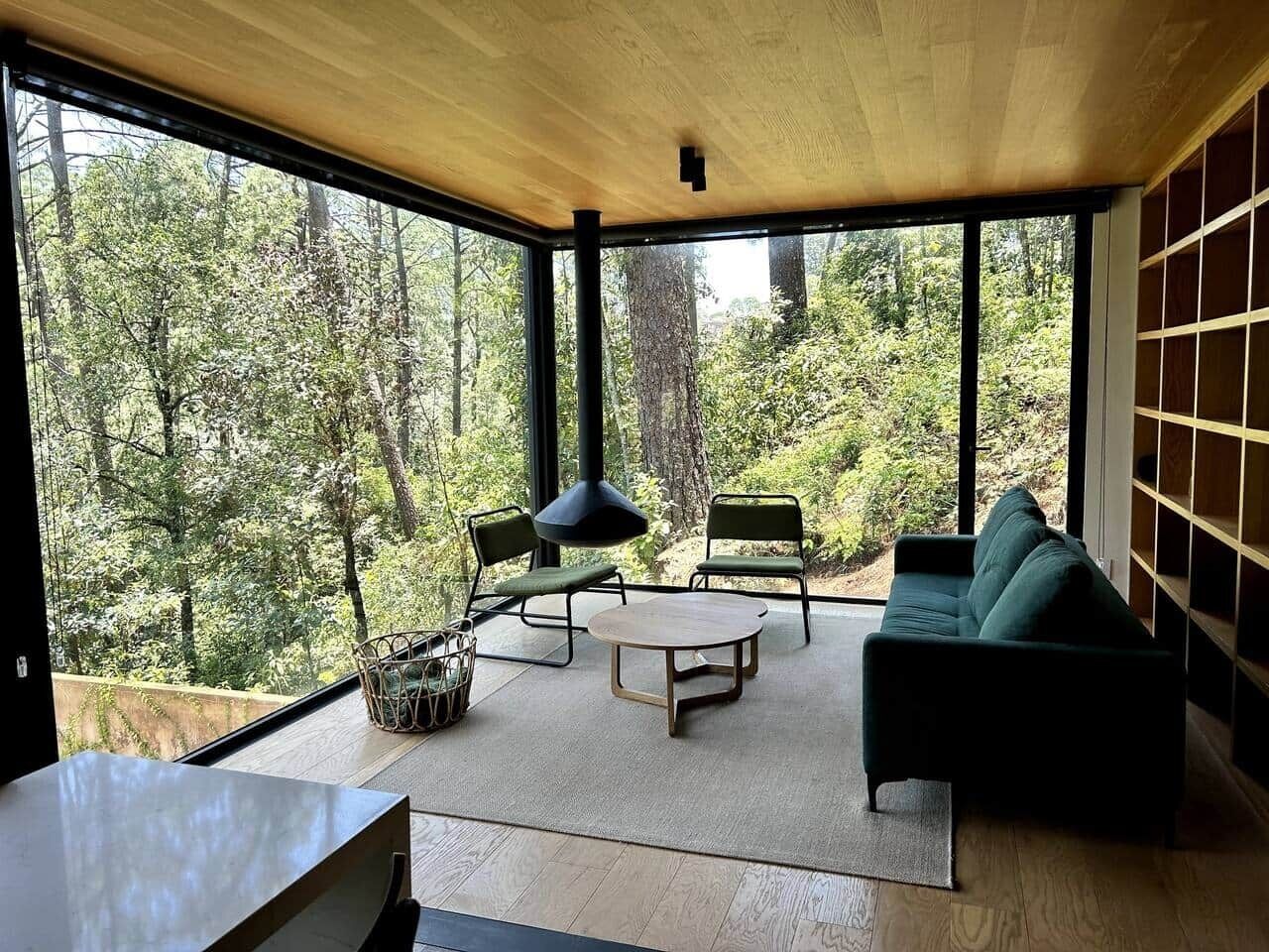 A modern interior with a large window, a sofa, two chairs, a table, and a hanging light fixture.