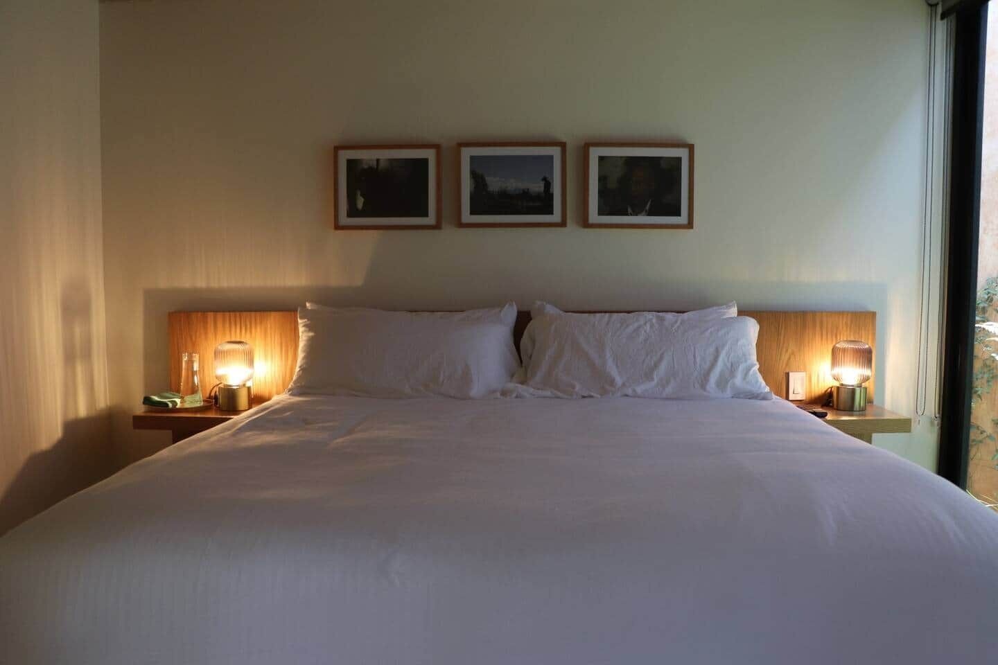 Una camera d'albergo con un letto grande, due lampade sui comodini e tre quadri appesi al muro.