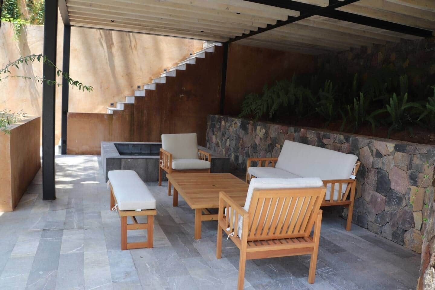 Eine Terrasse im Freien mit einem Holztisch und -stühlen, einer Bank und einer Steinmauer.