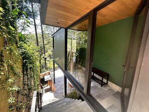 Un intérieur moderne avec un escalier menant à un balcon, un banc et une vue sur l’extérieur.