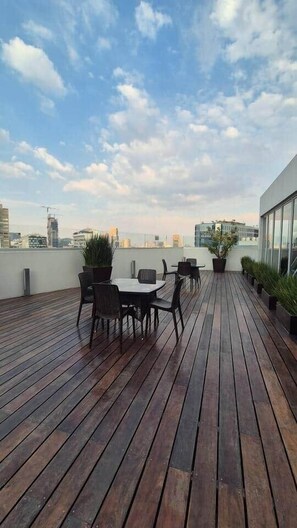 Eine Dachterrasse mit Holzdeck, einem Tisch mit Stühlen, Blumentöpfen und Blick auf den Stadtpanoramahorizont.