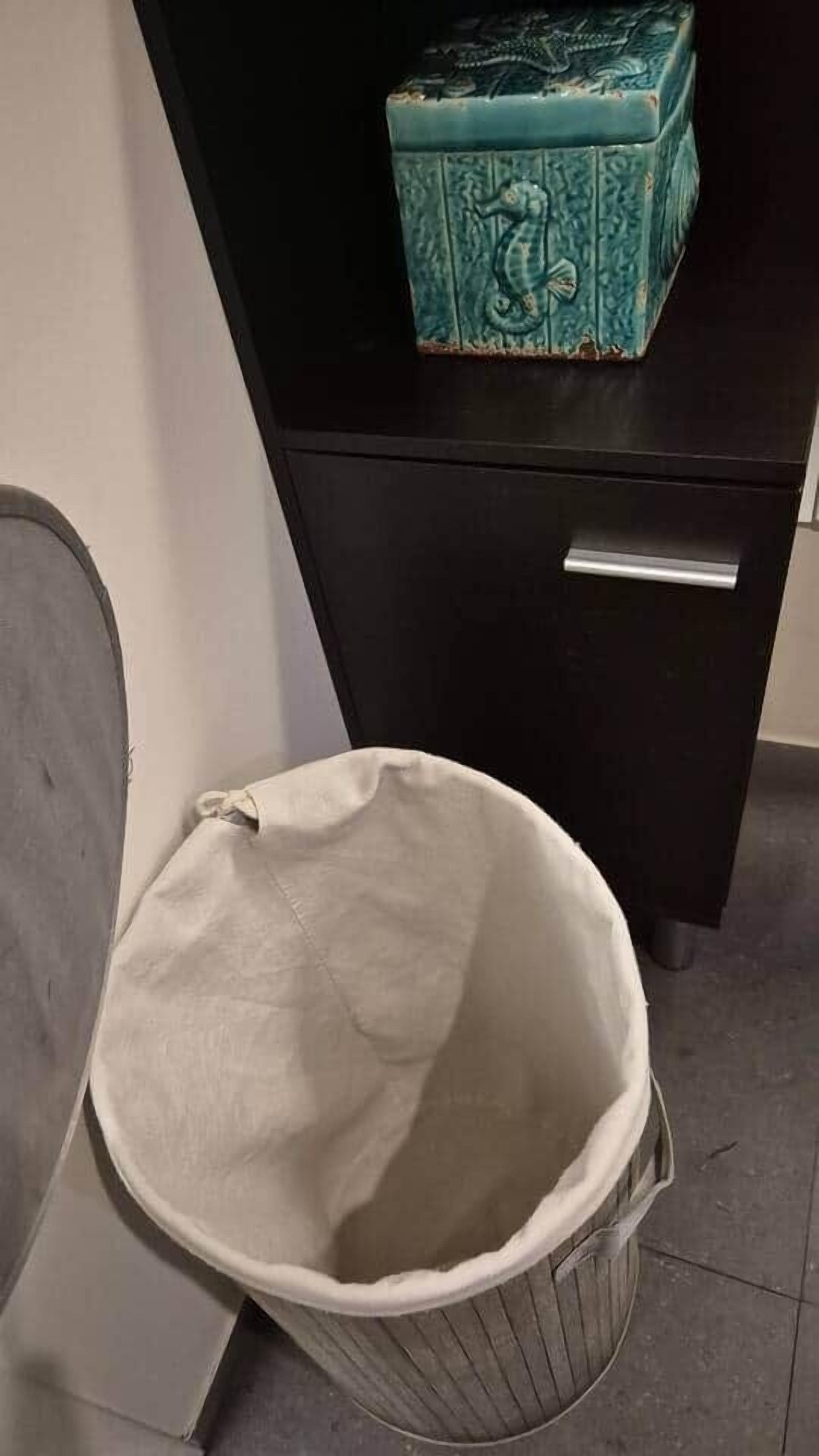 A white trash bin next to a black desk with a teal box on top.