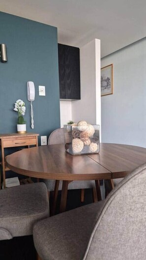 Ein Essbereich mit einem runden Tisch, Stühlen, einer Blumenvase, einem dekorativen Behälter und einem Telefon an der Wand.